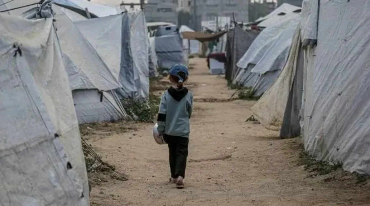 Child walking between shelters in a displacement camp, photographed from behind
